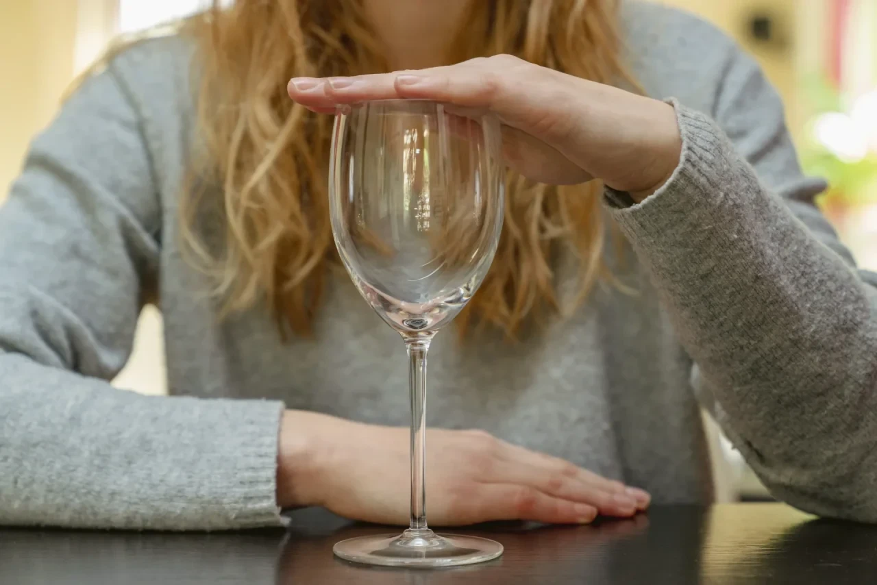 Frau sitzt vor Weinglas und hält das Glas mit der Hand zu
