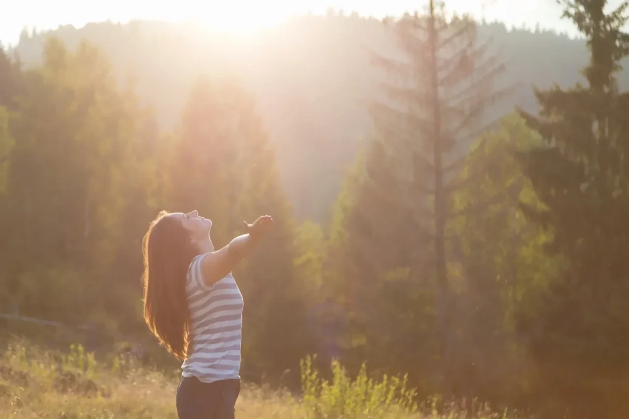 Frau steht im Wald in Sonnenstrahlen