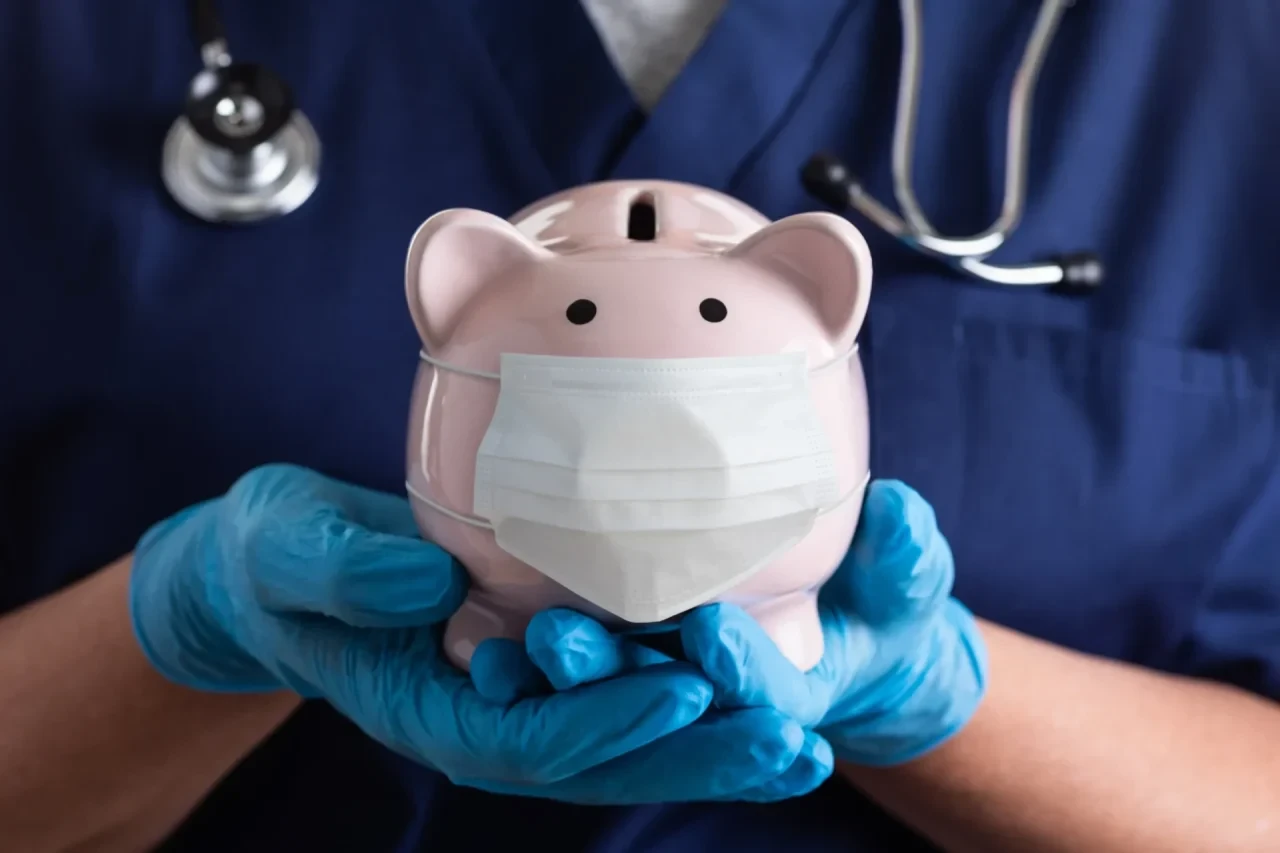 Arzt hält Sparschwein mit Mundschutz
