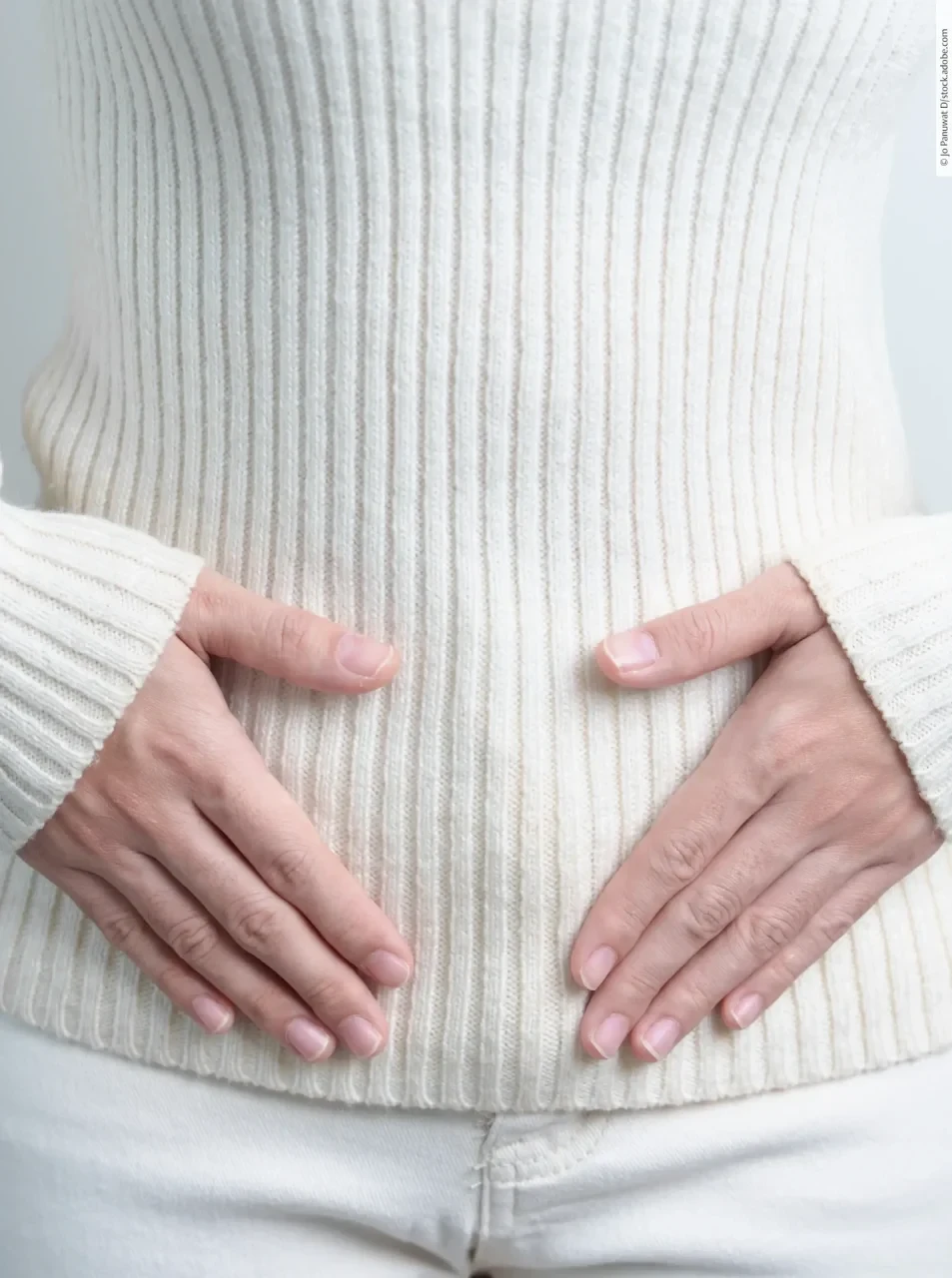 Frau im Pulli legt Hände auf den Bauch